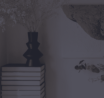 Black vase of dried flowers on a stack of books.