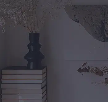 Black vase of dried flowers on a stack of books.