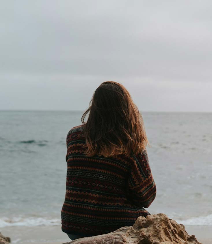 Woman in patterned sweater looking at ocean.