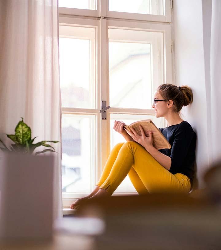 Woman in yellow pants reading a book on a window ledge.