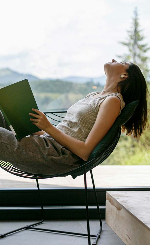 Woman relaxing with a book indoors by a mountain view.