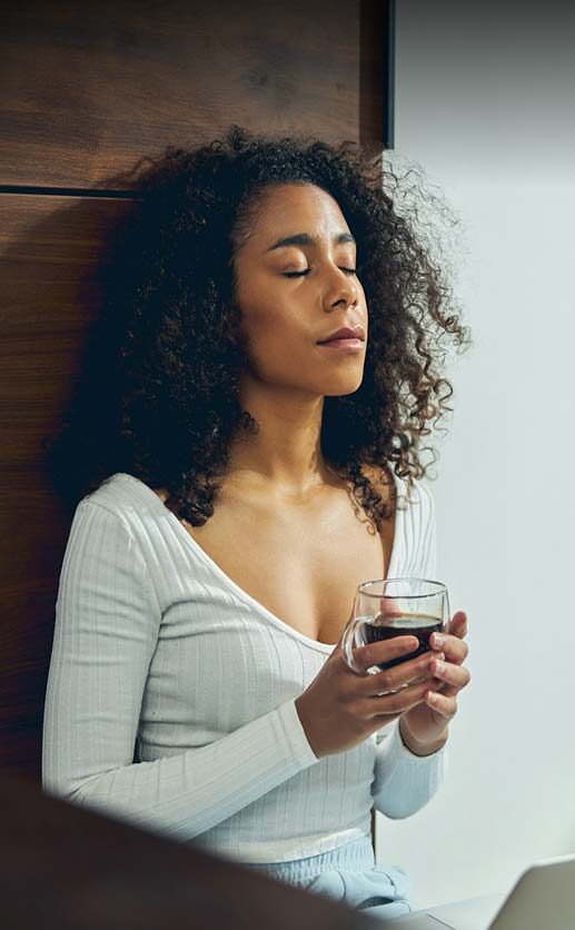 Woman with curly hair, eyes closed, holding a glass of coffee.