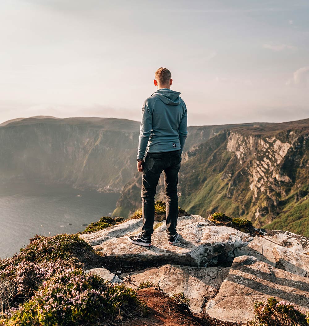 Man overlooking coastal cliffs from a rocky peak.