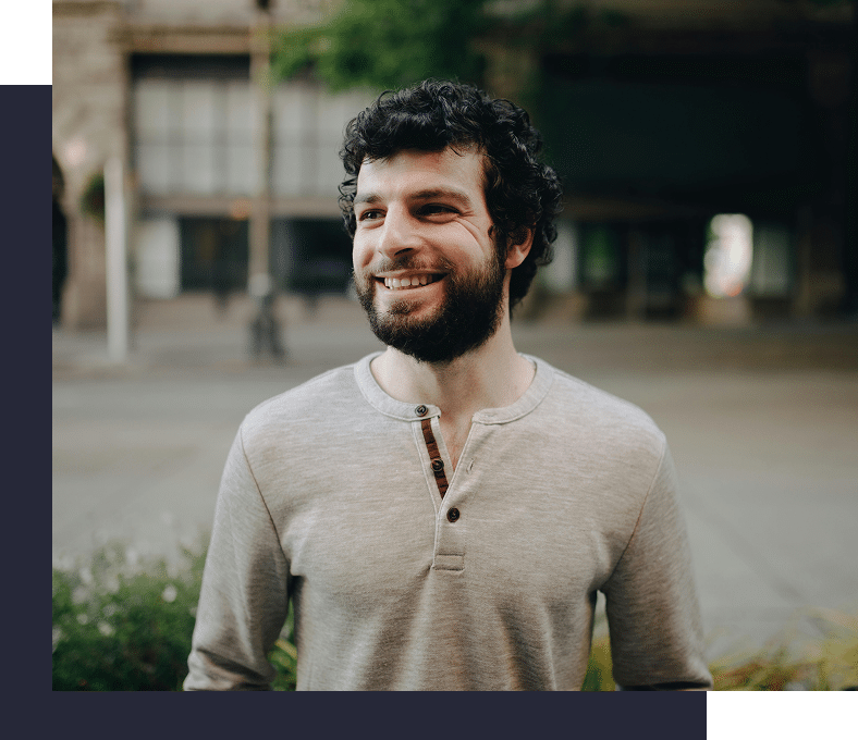 A man standing in front of a building, smiling, expressing confidence, ease, and emotional well-being in daily life.
