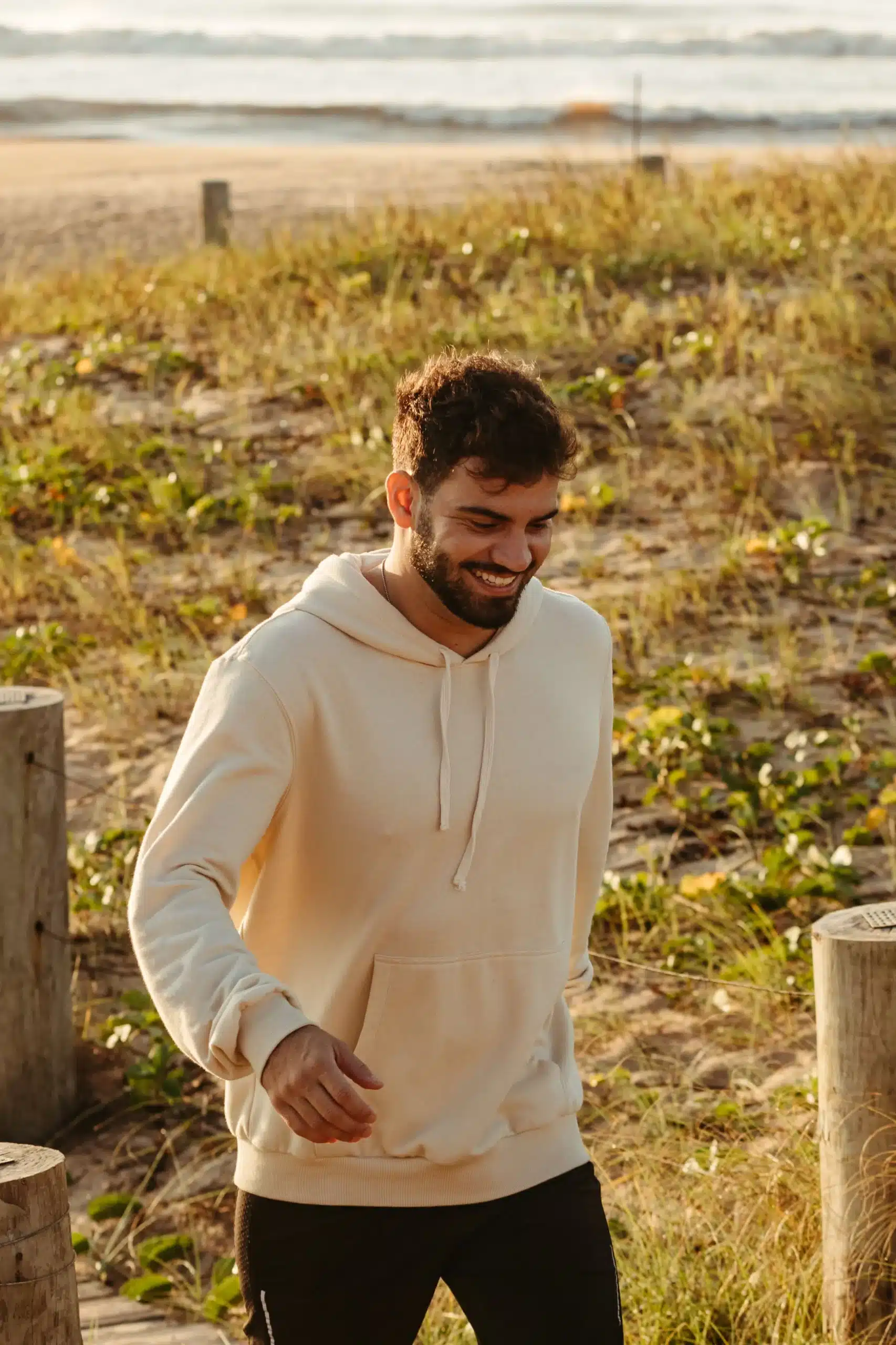 A happy man walking along a grassy dune path on the beach during golden hour.