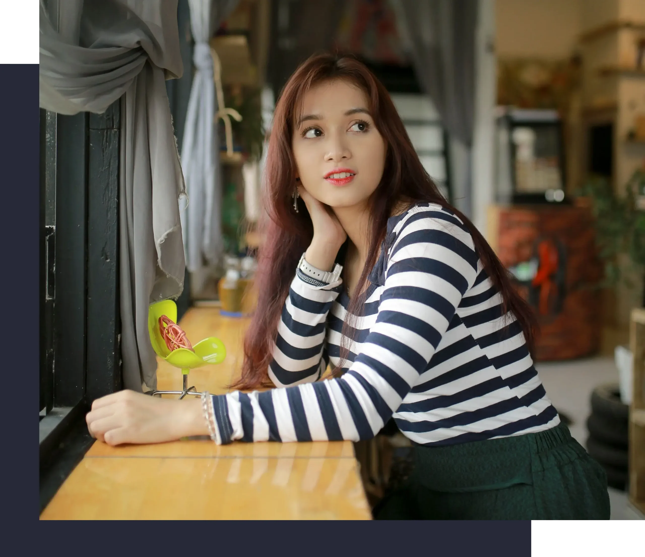 Woman wearing a navy and white striped top looking out the window while sitting at a wooden counter.